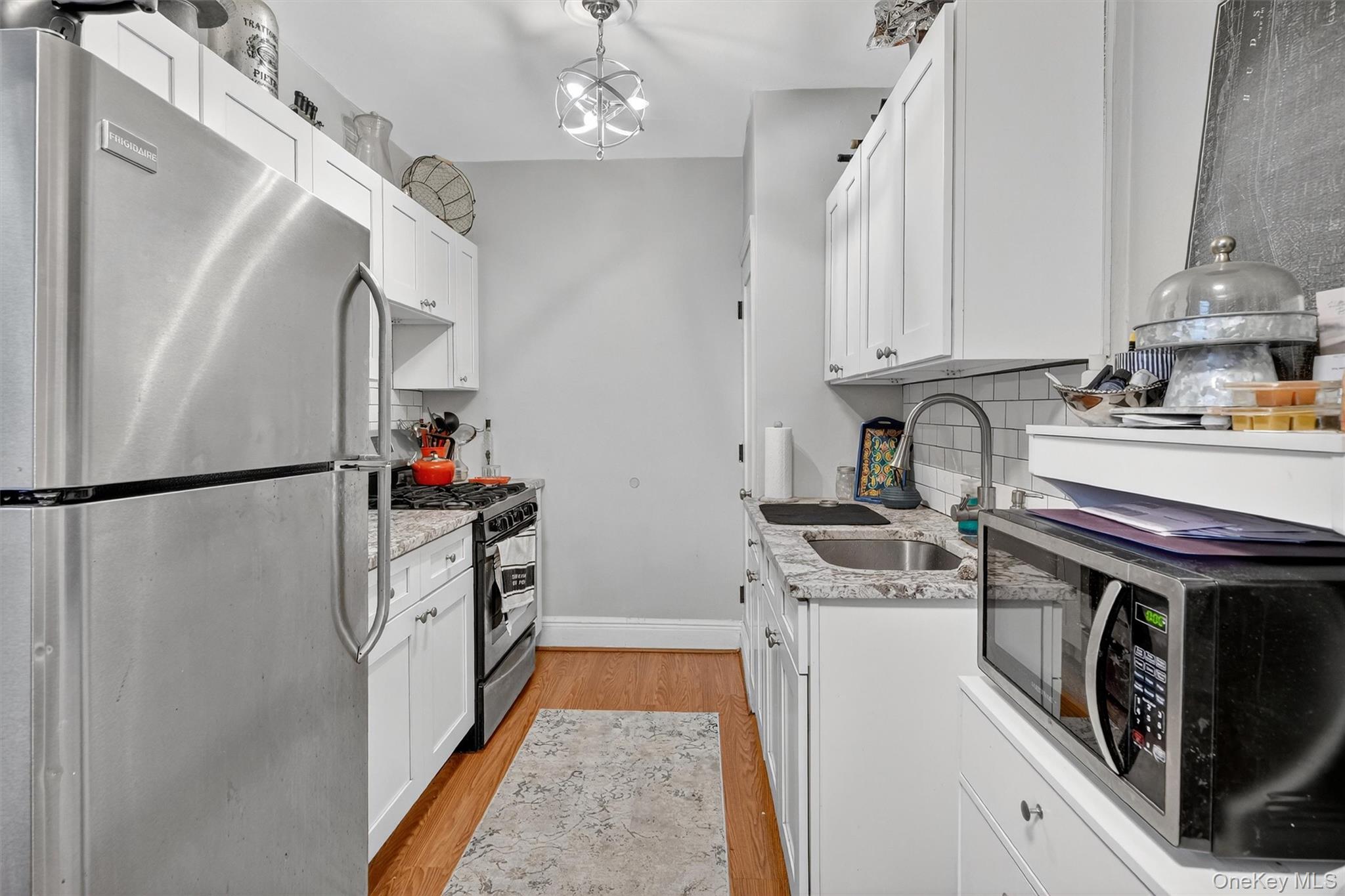 475 Bronx River Road, Unit 2D Yonkers, NY 10704 - Photo 15 of 27 Kitchen featuring stainless steel appliances, light stone counters, white cabinets, light wood-style flooring, and decorative backsplash
