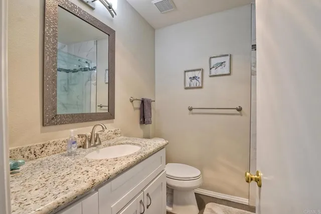 a bathroom with a granite countertop sink toilet and mirror