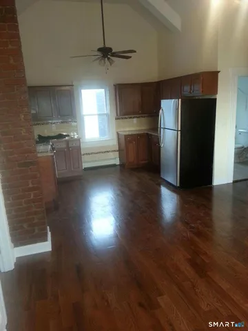 an empty room with wooden floor kitchen view and a refrigerator