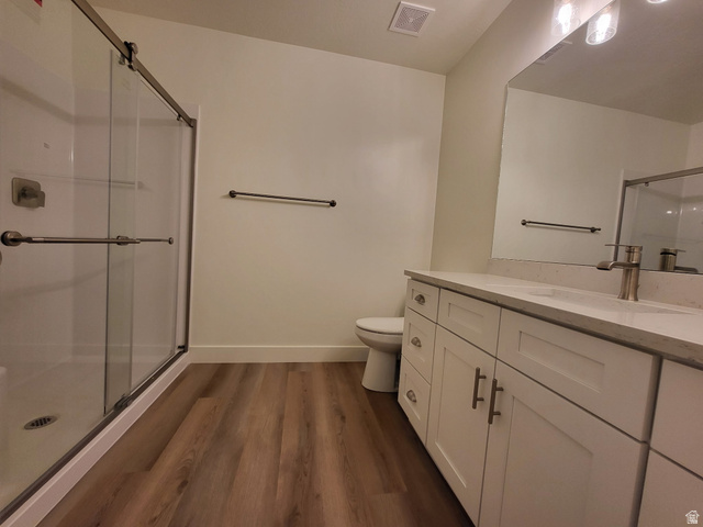 683 Kings Landing Tooele, UT 84074 - Photo 27 of 39 Bathroom featuring a double vanity with stone countertops, wood-finish flooring, a glass-enclosed shower, and a large mirror