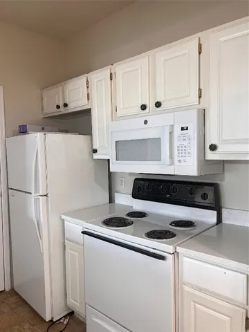 a white refrigerator freezer and a stove sitting inside of a kitchen with granite countertop white cabinets