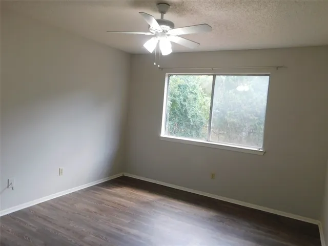 an empty room with wooden floor chandelier fan and windows