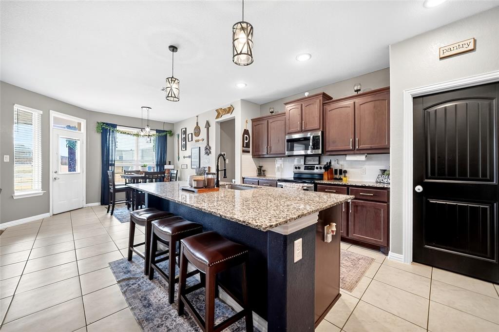 113 Ridgetop Trail Rhome, TX 76078 - Photo 11 of 32 Kitchen featuring a central island with a granite countertop, wood-finish cabinetry, stainless steel appliances, and tile flooring