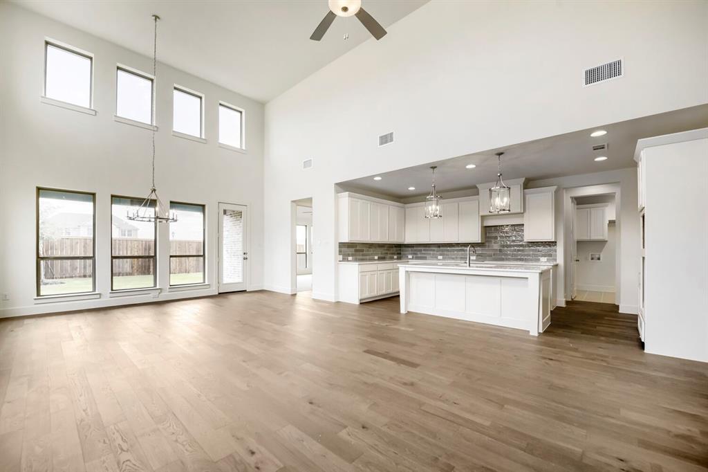 11548 Wulstone Road Haslet, TX 76052 - Photo 3 of 26 Spacious room featuring soaring ceilings, wood-finish flooring, and a kitchen with white cabinetry, a large island, and subway tile backsplash