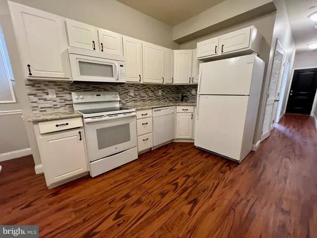 a kitchen with wooden floors white appliances white cabinets and wooden floors