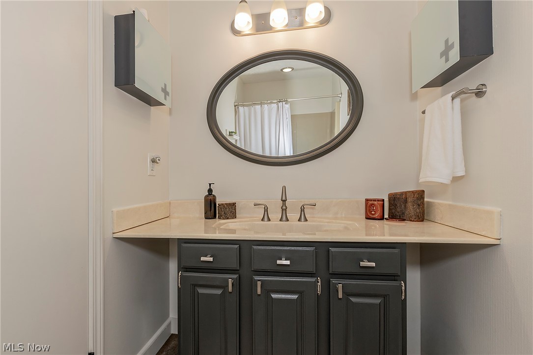 11292 Butternut Road Chardon, OH 44024 - Photo 29 of 49 Bathroom vanity featuring a light-toned countertop with an integrated sink, dark gray cabinetry with brushed nickel hardware, an oval mirror, and a three-light fixture