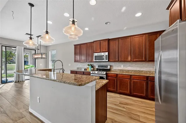 a kitchen with stainless steel appliances granite countertop a sink a stove a refrigerator cabinets and living room view