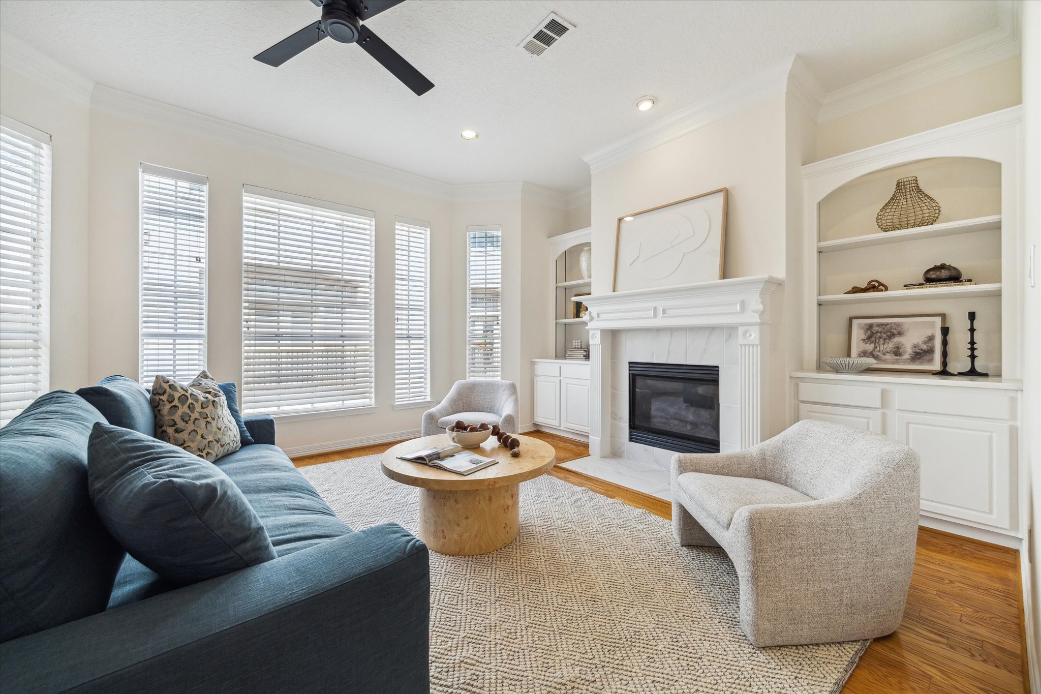 909 Reinicke Street Houston, TX 77007 - Photo 2 of 19 The living area is characterized by ample space and abundant natural light, featuring hardwood flooring, newly installed tile surrounding the gas fireplace, and a recently installed ceiling fan. The space includes built-in adjustable shelving and storage.