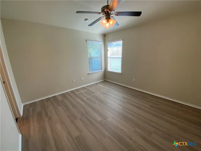 an empty room with wooden floor fan and windows