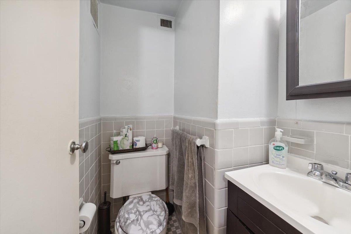 3 Fordham Hill Ovl, Unit 10B Bronx, NY 10468 - Photo 11 of 33 Half bathroom featuring tile walls, vanity, toilet, and a wainscoted wall