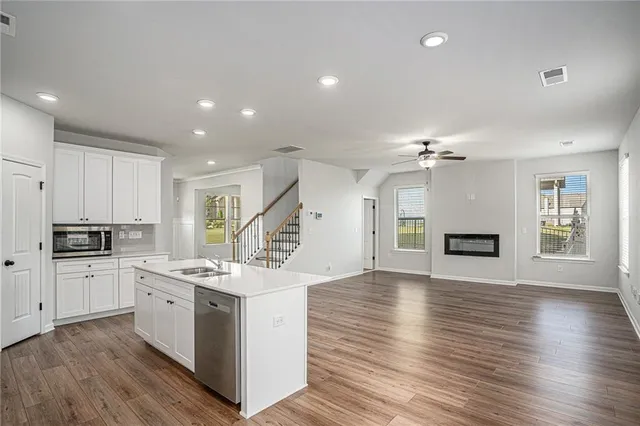 a large white kitchen with stainless steel appliances granite countertop a stove top oven a refrigerator a sink and white cabinets with wooden floor