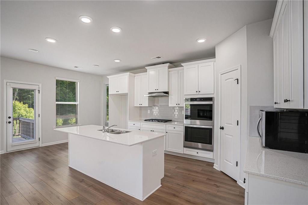 953 Mystic Way Hampton, GA 30228 - Photo 16 of 51 a large white kitchen with stainless steel appliances granite countertop a stove top oven a refrigerator a sink and white cabinets with wooden floor