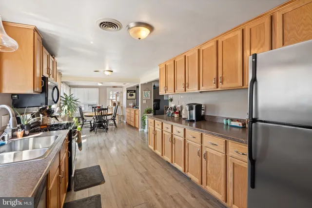 a kitchen with granite countertop a refrigerator a sink dishwasher a stove top oven a dining table and chairs with wooden floor