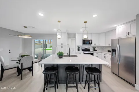 a kitchen with granite countertop a dining table chairs refrigerator and cabinets
