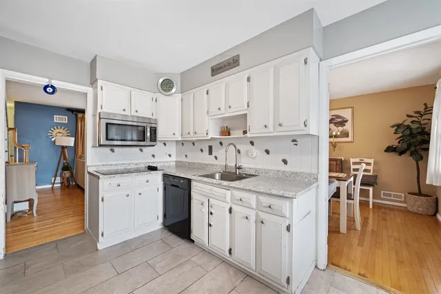 a kitchen with stainless steel appliances granite countertop a stove top oven a sink a refrigerator and white cabinets with wooden floor