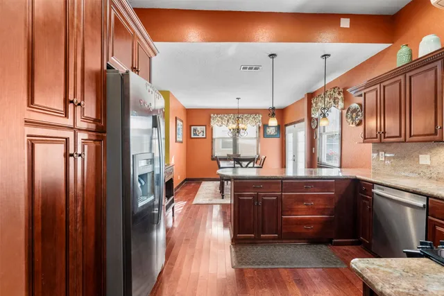 a large kitchen with stainless steel appliances granite countertop a refrigerator a sink dishwasher a dining table and chairs with wooden floor