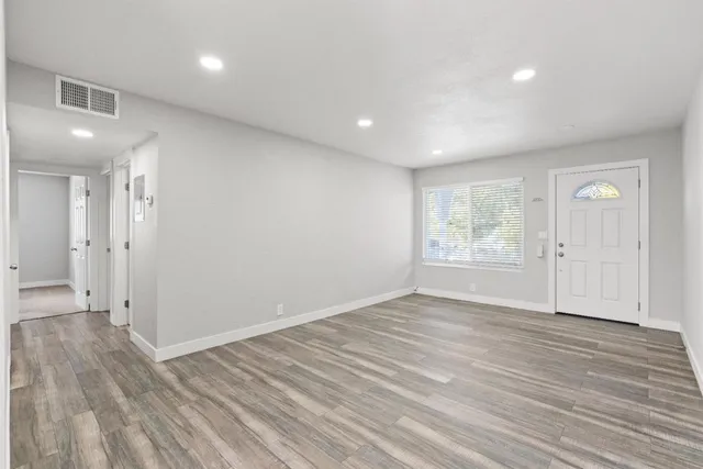 a view of an empty room with wooden floor and a window