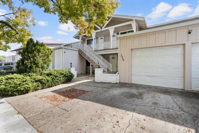 a view of a white house with a large tree and wooden fence