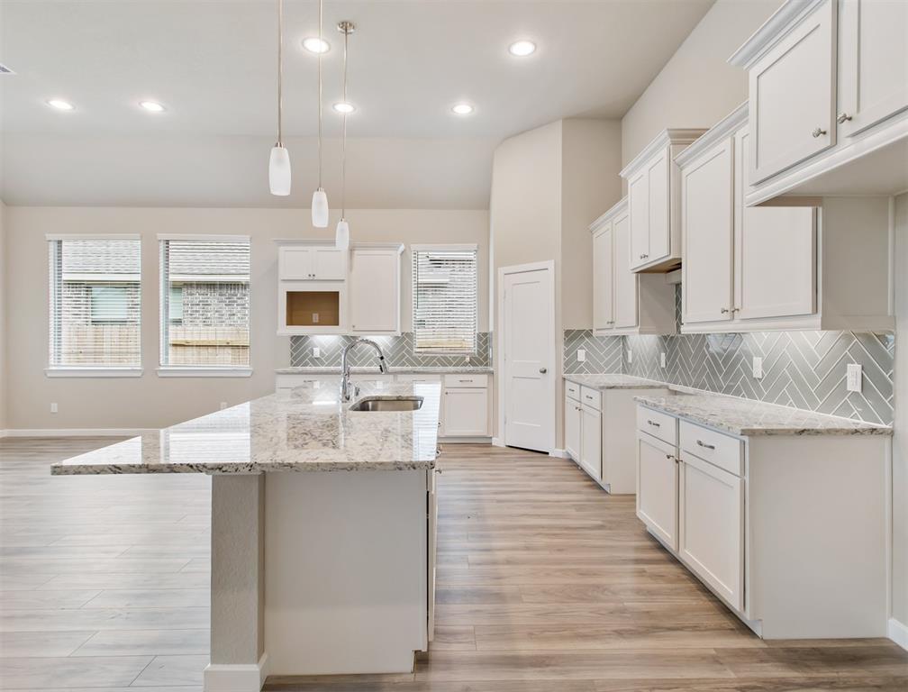 a large kitchen with granite countertop a sink large white cabinets and a granite countertops with wooden floor