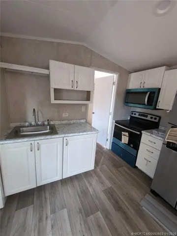 a kitchen with granite countertop a stove top oven a sink dishwasher and white cabinets with wooden floor