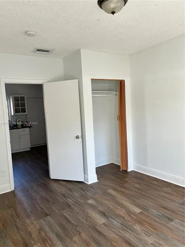 an empty room with wooden floor and a kitchen