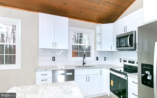 a kitchen with stainless steel appliances granite countertop a sink dishwasher stove and white cabinets with wooden floor