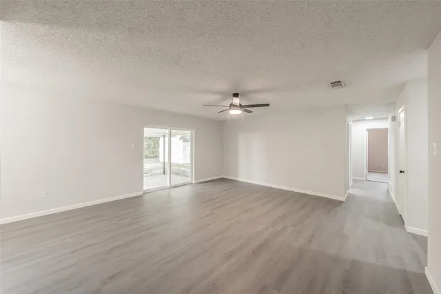 an empty room with wooden floor ceiling fan and windows