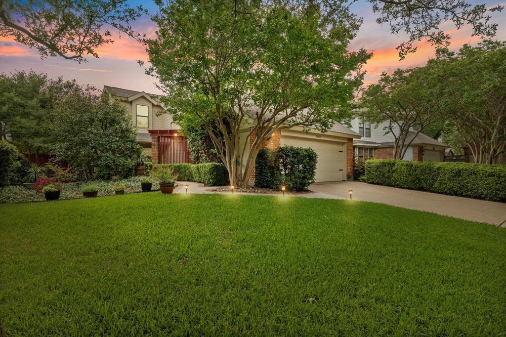 View of property hidden behind natural elements featuring brick siding, a yard, driveway, and a garage