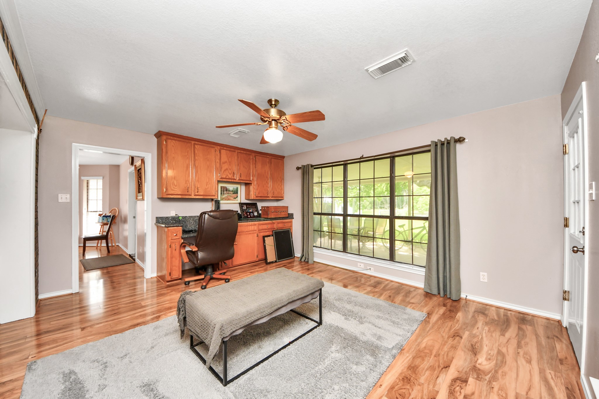 12746 Roy Road Pearland, TX 77581 - Photo 31 of 47 This room features a spacious, bright area with large windows and wooden flooring. It includes a built-in desk with cabinetry, a ceiling fan, and neutral-toned walls, creating a cozy and functional space.