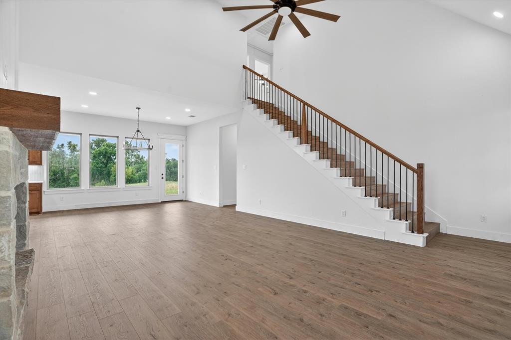 225 Kilkenny Road Poolville, TX 76487 - Photo 6 of 36 Spacious living area featuring wood-finish flooring, a prominent stone-clad fireplace with a wood mantle, and a staircase with wood handrails and black iron balusters