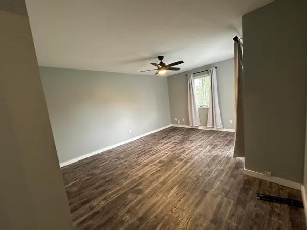 an empty room with wooden floor ceiling fan and window
