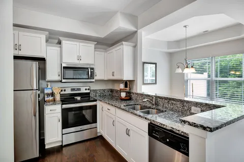 a kitchen with granite countertop white cabinets appliances and a window