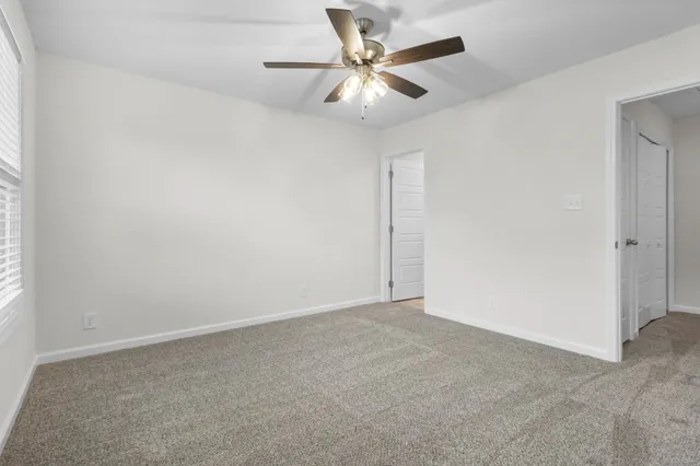 an empty room with a chandelier fan and windows