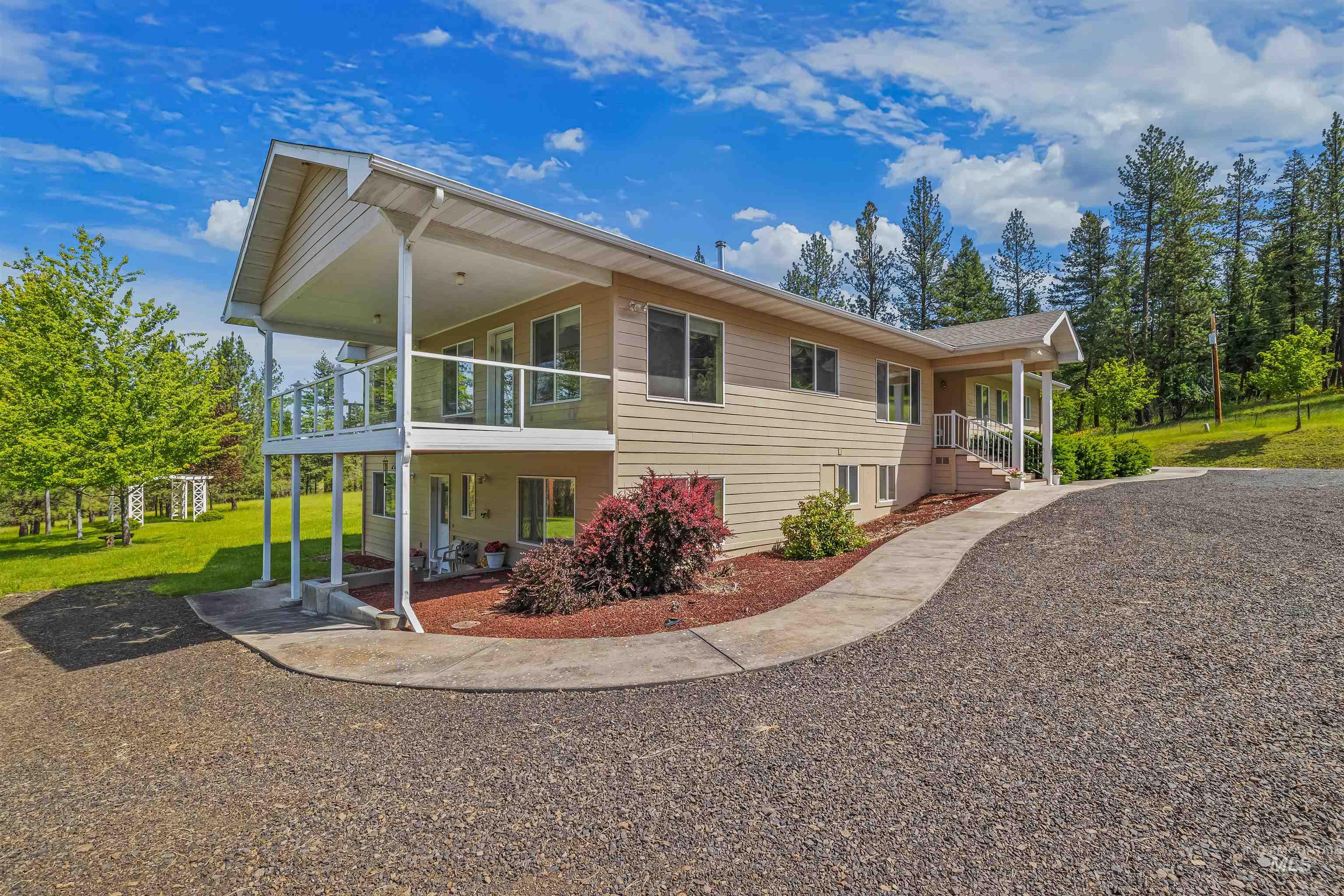 743 Wall Crk Road Stites, ID 83552 - Photo 3 of 48 Two-story property featuring tan siding, a covered upper-level deck with glass railings, a covered lower-level patio, a curved concrete pathway, and a gravel driveway