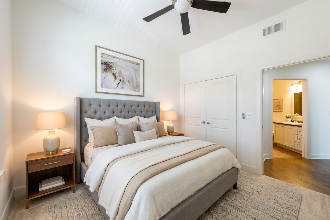 1010 Rosine Street, Unit 29 Houston, TX 77019 - Photo 3 of 16 This bedroom features a cozy layout with a plush, tufted bed and neutral-toned bedding. It includes a bedside table with a lamp, a ceiling fan, and double doors leading to an en-suite bathroom with ample counter space. The room is bright and inviting, perfect for relaxation. (Virtual Staging)