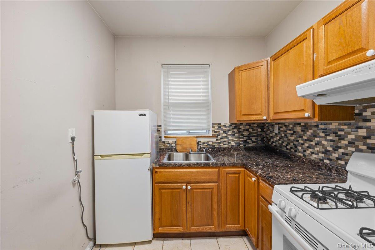 2953 Harding Avenue Bronx, NY 10465 - Photo 13 of 29 Kitchen with white appliances, brown cabinetry, light tile patterned floors, under cabinet range hood, and decorative backsplash