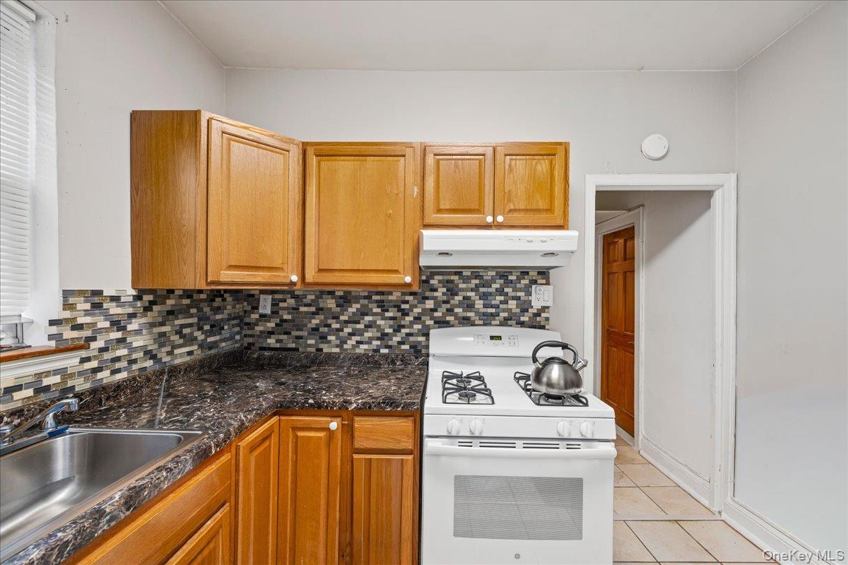 2953 Harding Avenue Bronx, NY 10465 - Photo 14 of 29 Kitchen with white range with gas cooktop, under cabinet range hood, brown cabinets, light tile patterned floors, and dark stone counters