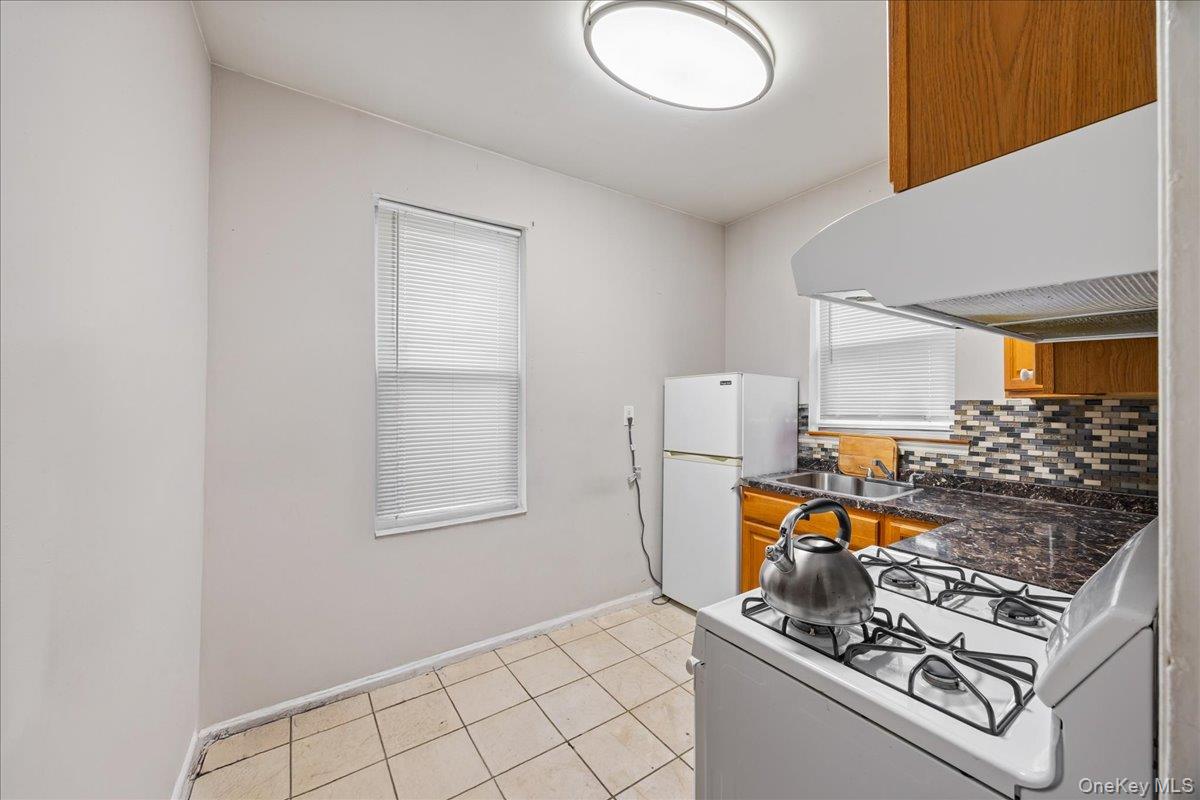 2953 Harding Avenue Bronx, NY 10465 - Photo 15 of 29 Kitchen featuring white appliances, under cabinet range hood, backsplash, brown cabinetry, and light tile patterned floors