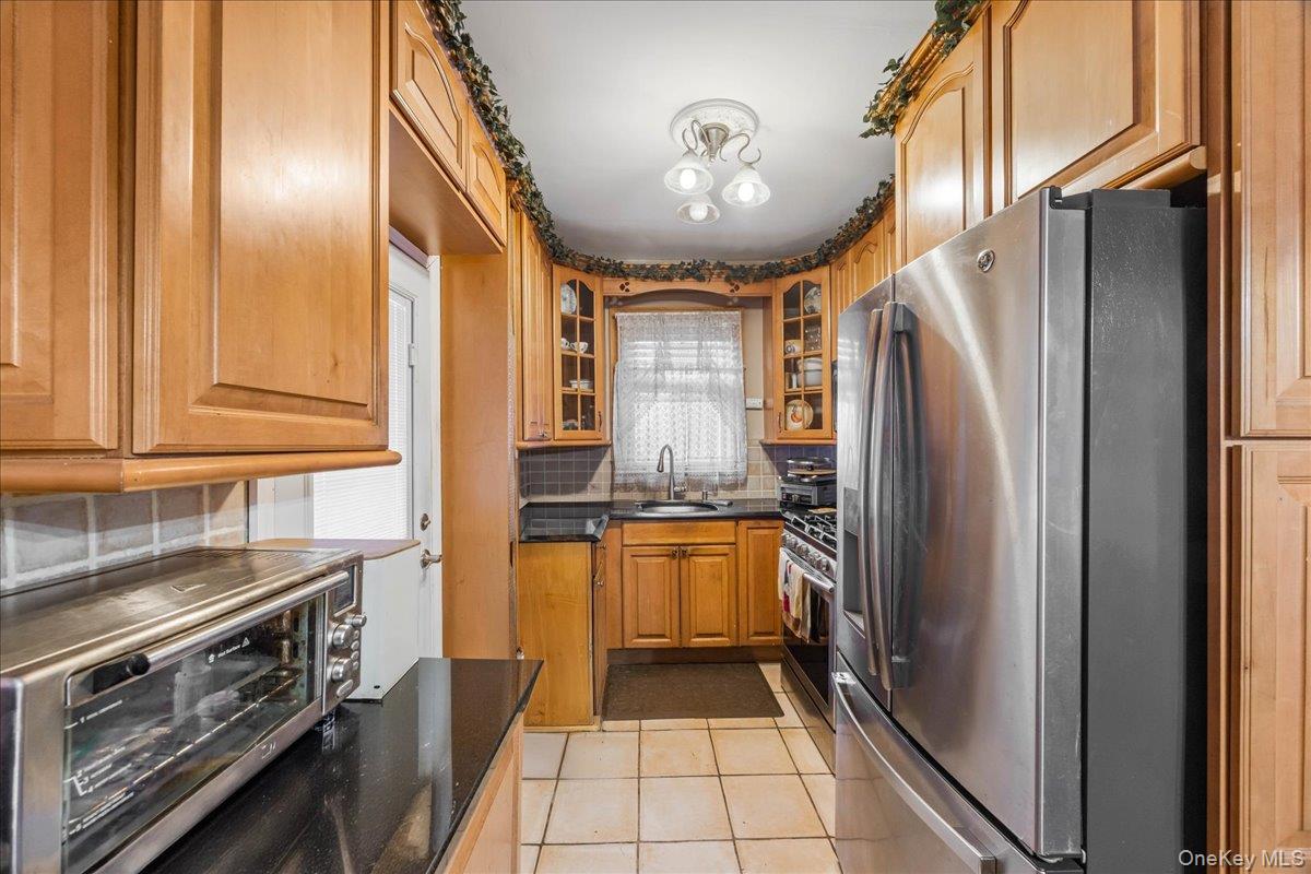 2953 Harding Avenue Bronx, NY 10465 - Photo 6 of 29 Kitchen with stainless steel appliances, decorative backsplash, brown cabinets, light tile patterned floors, and glass insert cabinets