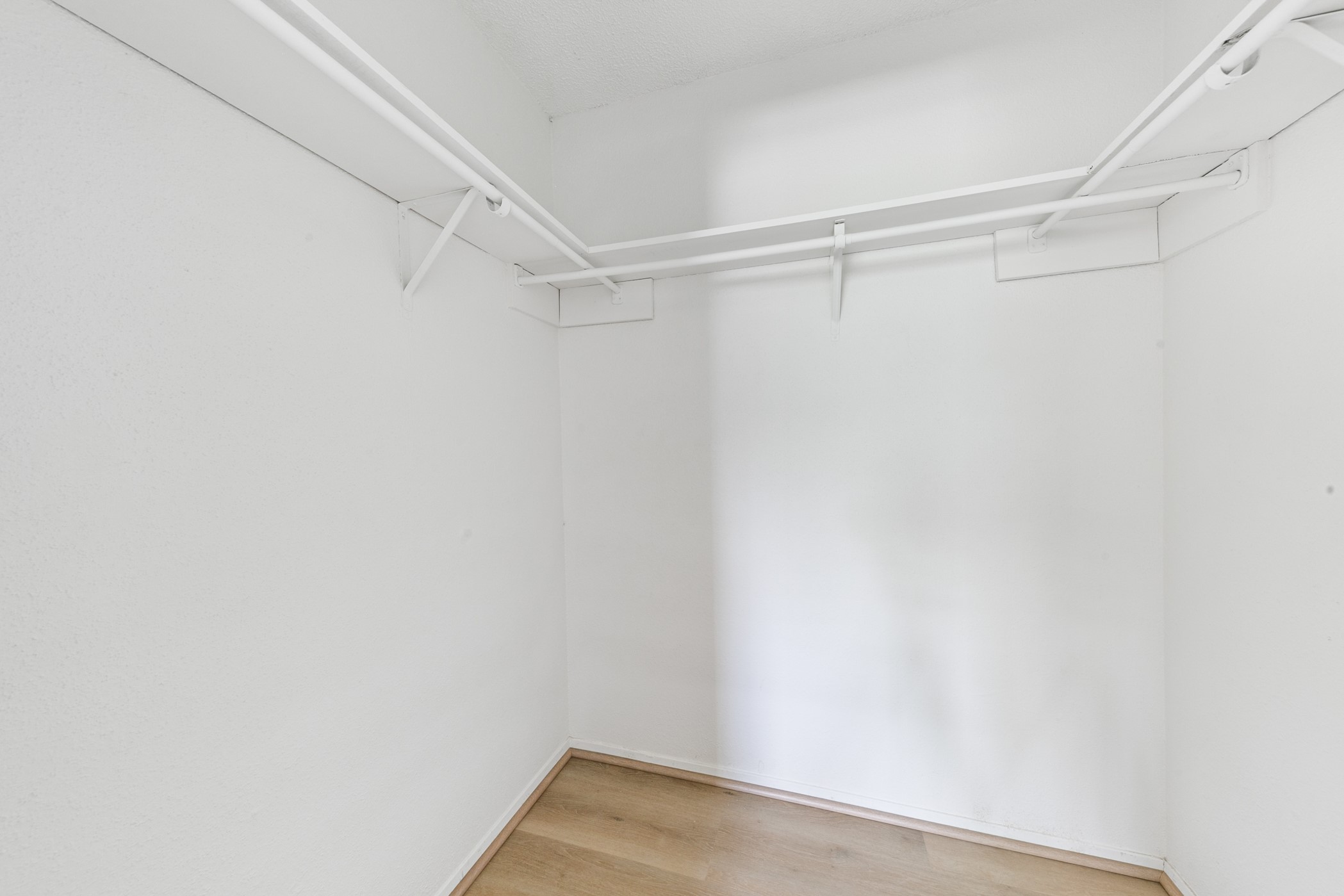 700 Lyle W Avenue, Unit D Cleveland, TX 77327 - Photo 14 of 16 This photo shows a spacious walk-in closet with white walls and two hanging rods, featuring light wood flooring, ideal for ample storage and organization.