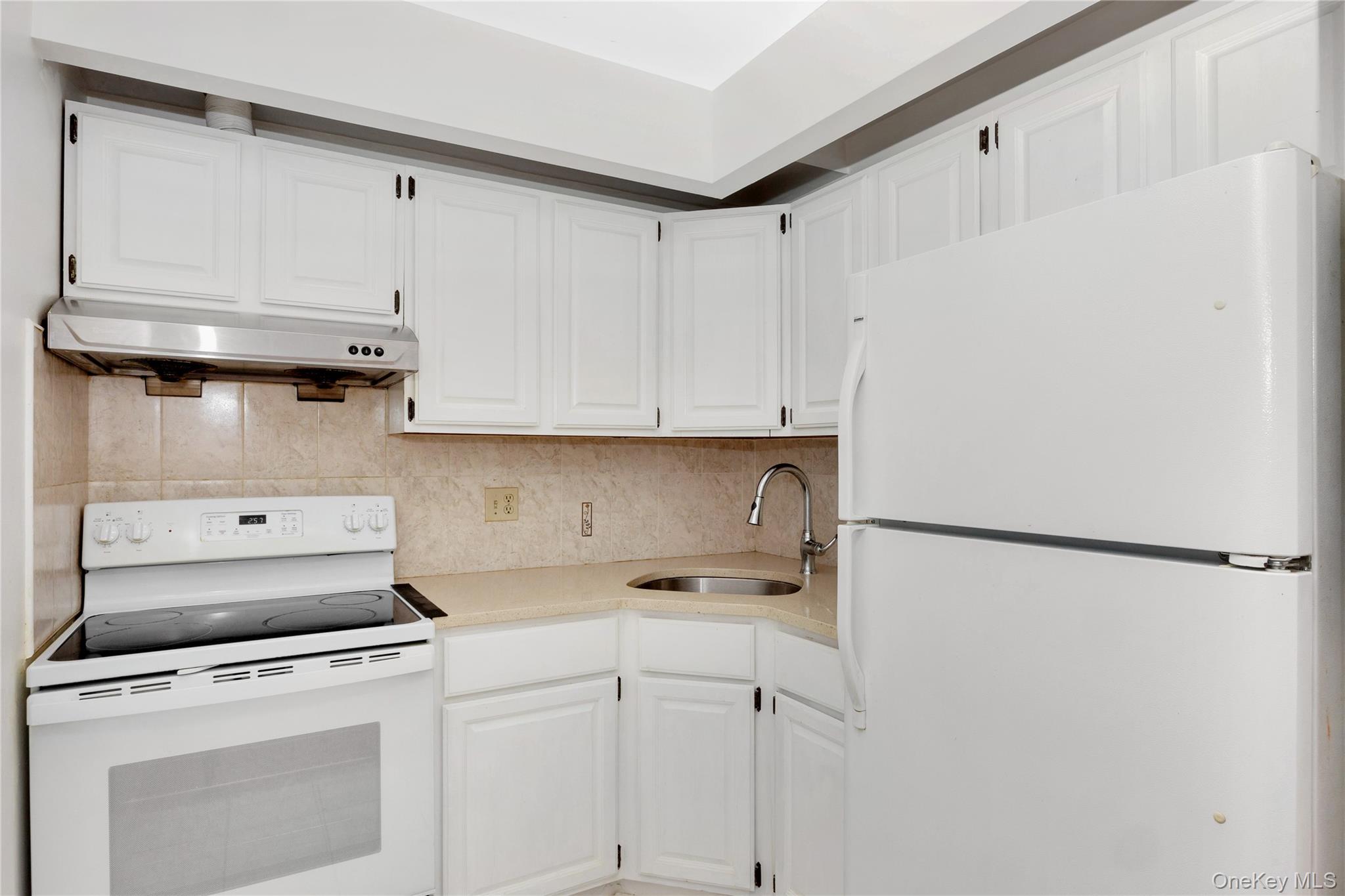 41-23 76th Street, Unit 2B Queens, NY 11373 - Photo 5 of 8 Kitchen with white appliances, under cabinet range hood, white cabinets, decorative backsplash, and light countertops