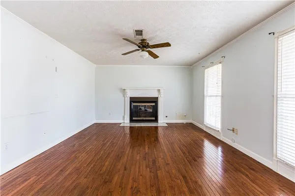 an empty room with wooden floor ceiling fan and windows