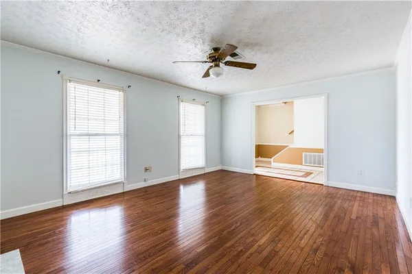 an empty room with wooden floor chandelier fan and windows