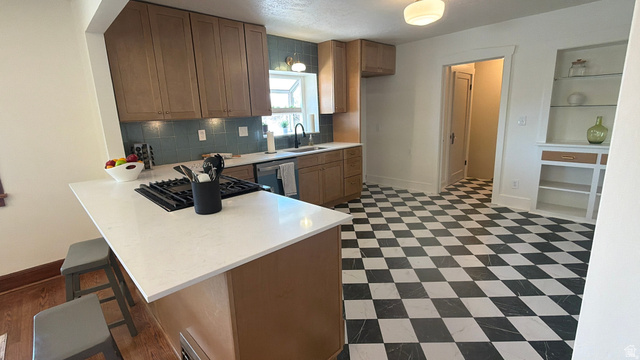 4883 South Center Street Murray, UT 84107 - Photo 6 of 32 Kitchen featuring a checkerboard floor, recessed lighting, light wood-finish cabinetry, a white countertop island with a built-in cooktop, and a blue tile backsplash