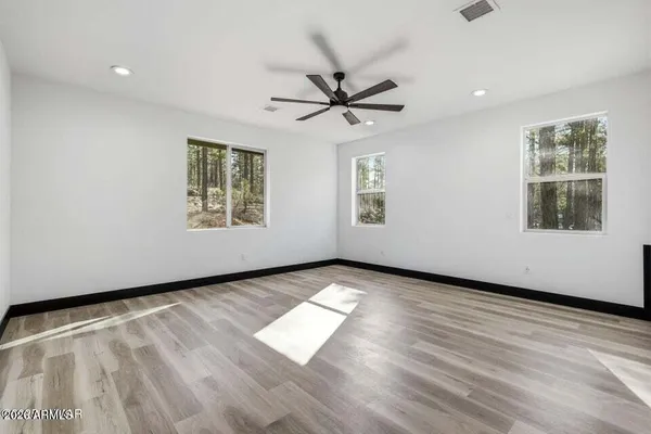 a view of an empty room with wooden floor and a ceiling fan