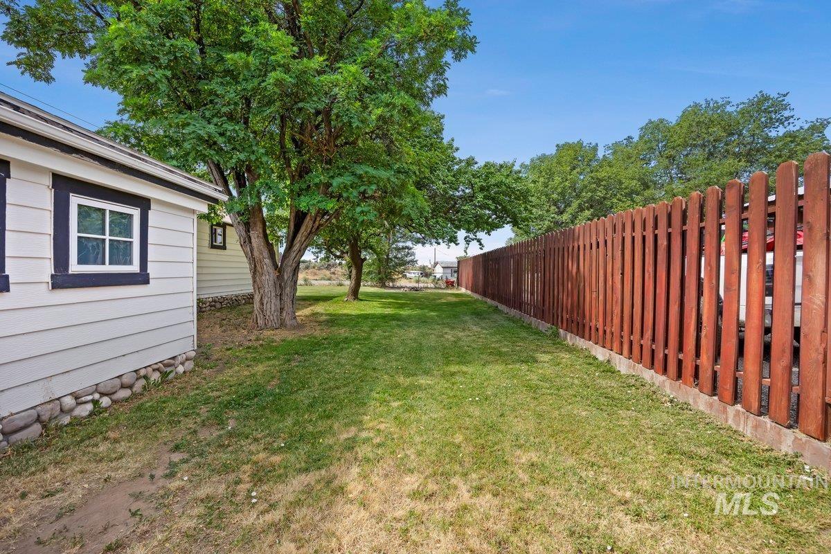 418 South Date Street Shoshone, ID 83352 - Photo 25 of 36 Expansive green space featuring a wood privacy fence, mature trees, and a building exterior with horizontal siding and stone foundation