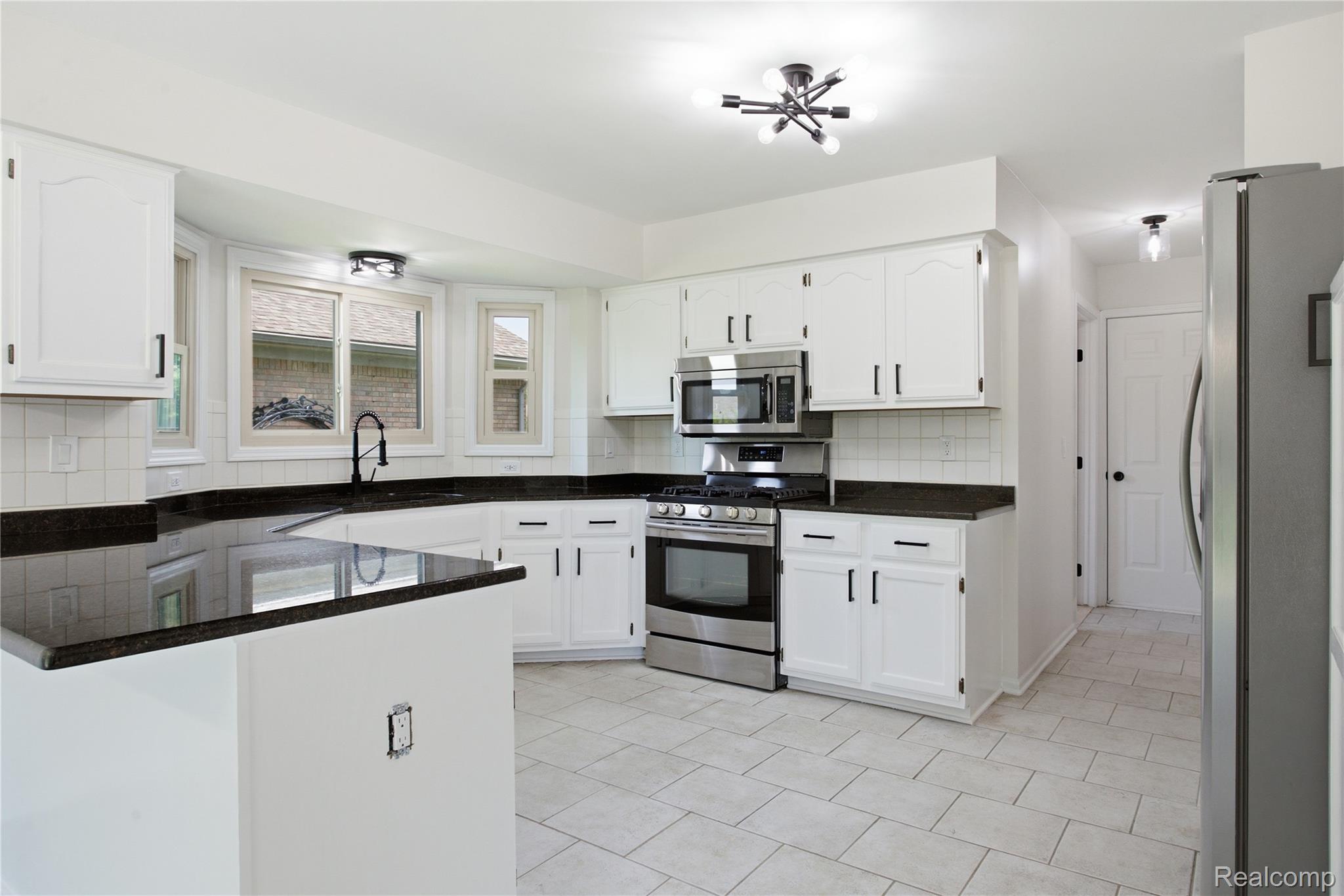 52658 Stag Ridge Drive Macomb, MI 48042 - Photo 8 of 28 Kitchen featuring white cabinetry, dark countertops, a stainless steel gas range, a coordinating microwave, and light-toned tile flooring