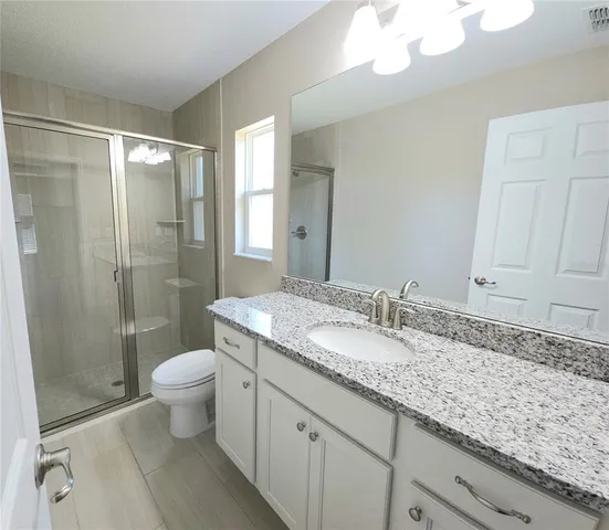 a bathroom with a granite countertop sink a toilet a mirror and shower