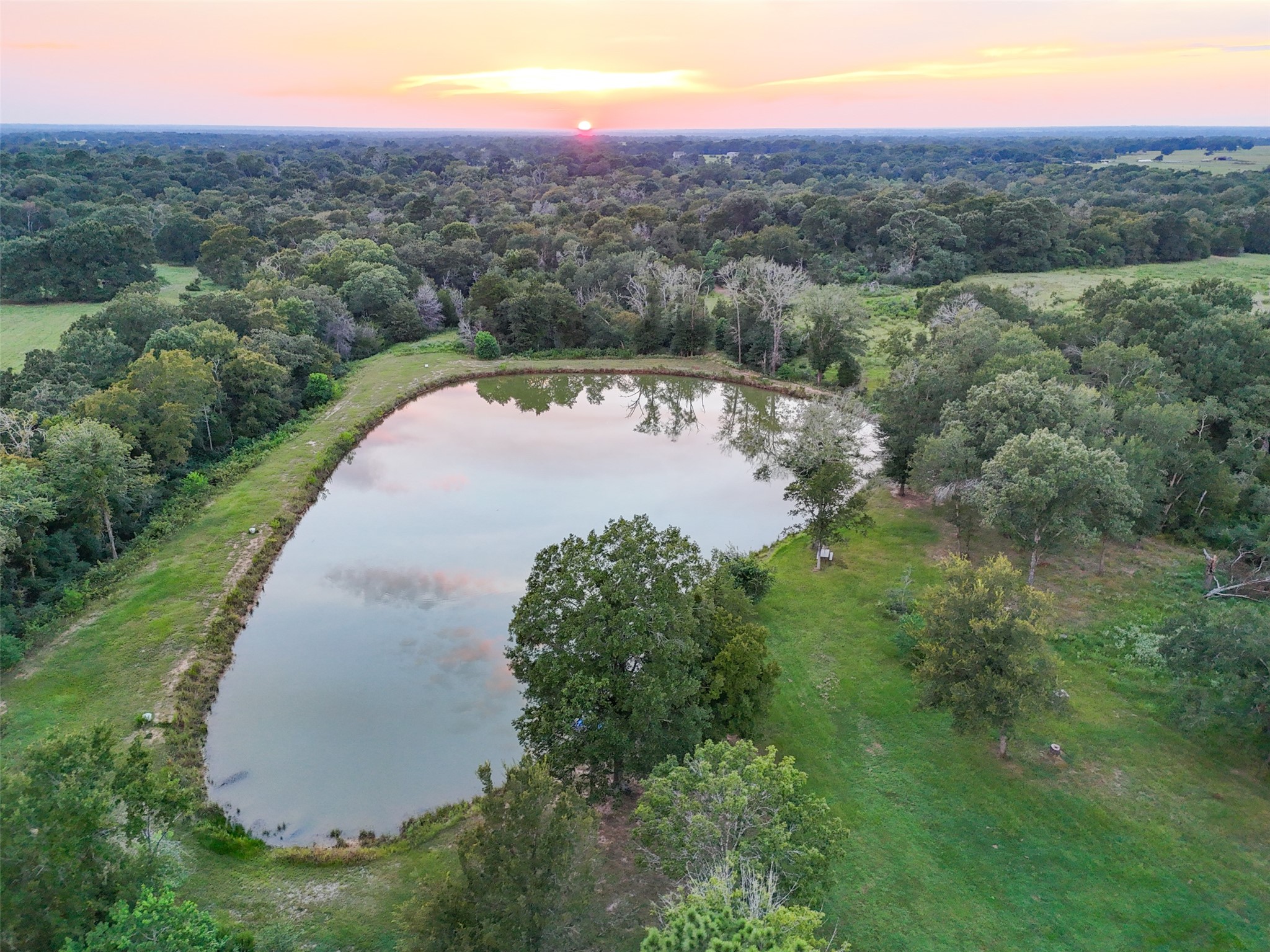 27201 Double Culvert Road Hempstead, TX 77445 - Photo 44 of 49 Picturesque pond reflects the sunset sky, creating a tranquil backdrop surrounded by open green space.