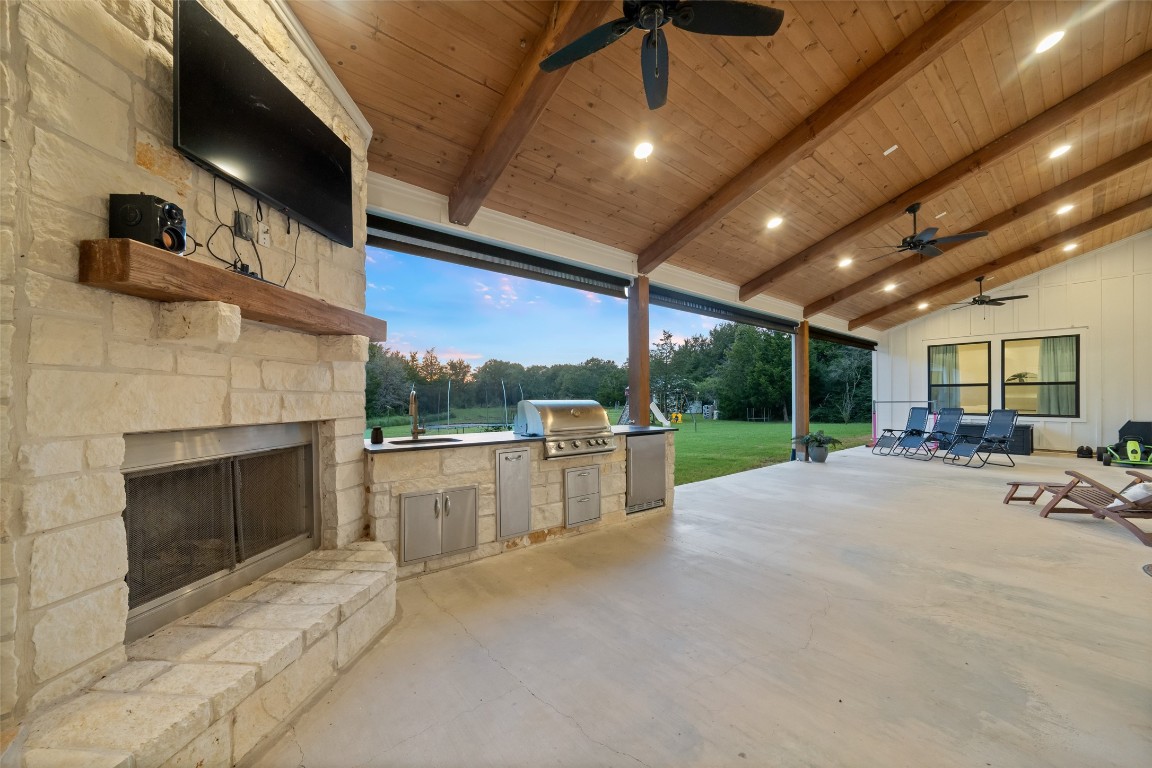 27201 Double Culvert Road Hempstead, TX 77445 - Photo 8 of 49 The outdoor kitchen is fully equipped with built-in grill, sink, refrigerator, and stone fireplace under a wood-paneled ceiling. Retractable shades enhance year-round enjoyment.
